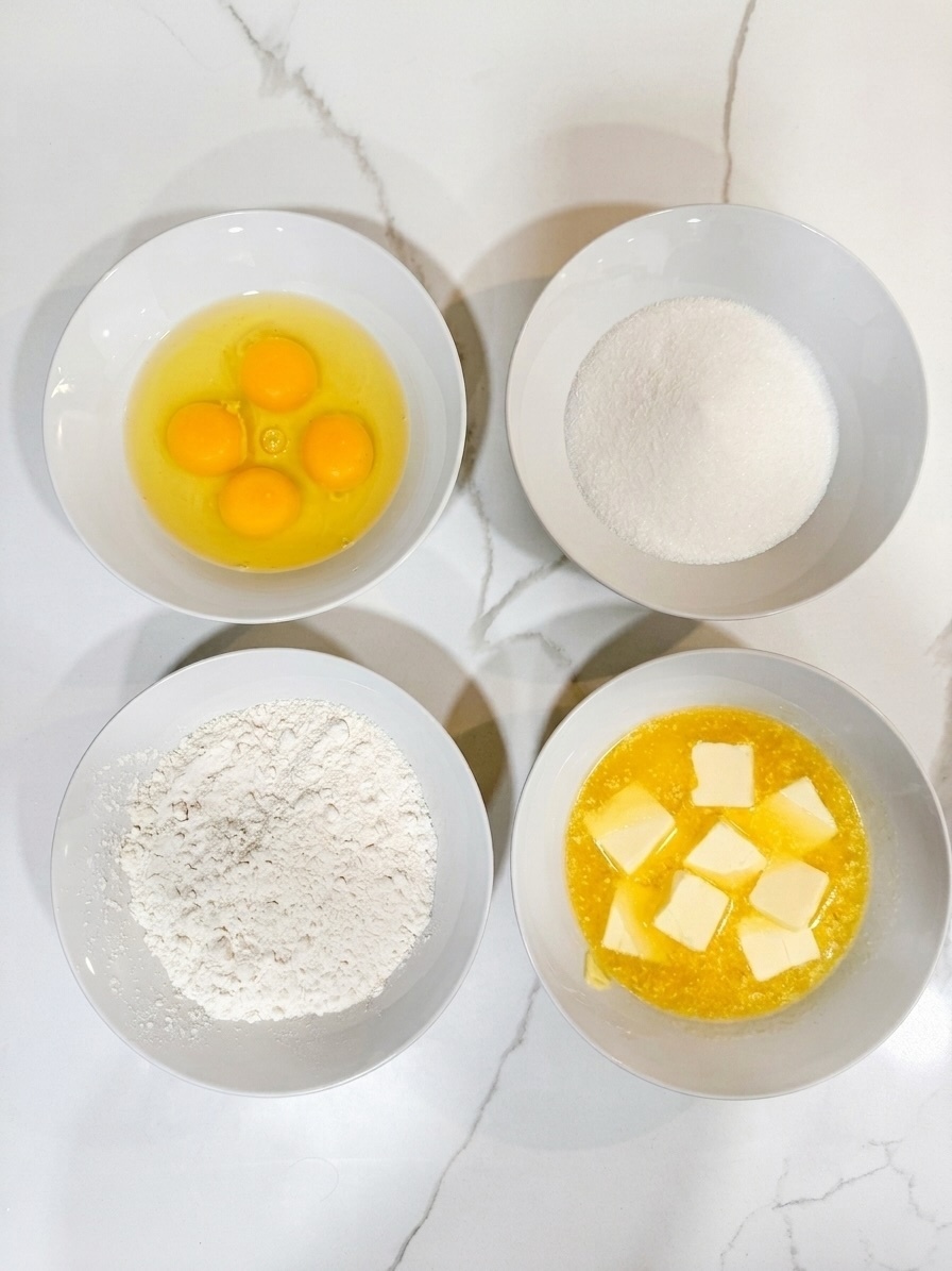 Four bowls holding eggs, sugar, flour, and melted butter in equal parts